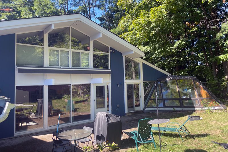 A three-story olive-green Victorian house with a turret and a wrap-around porch.