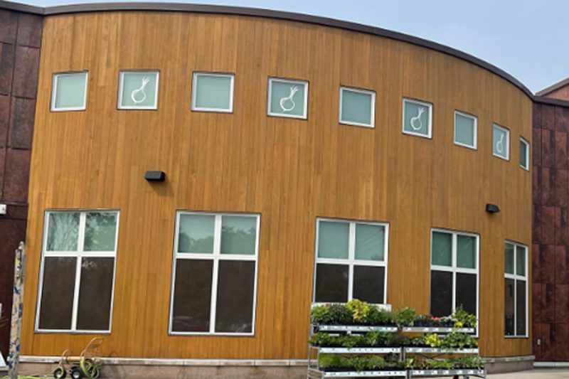A modern two-story building with a curved wood-paneled facade and small onion icons on the windows.