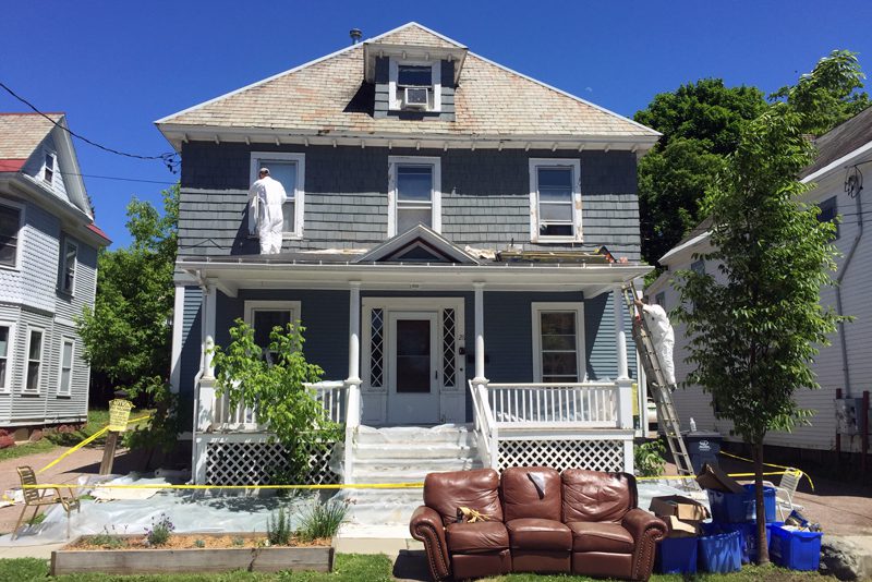 2 men in white painters outfits painting the exterior of a house blue