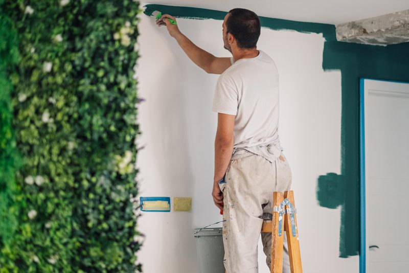 Man on a ladder painting a white wall green