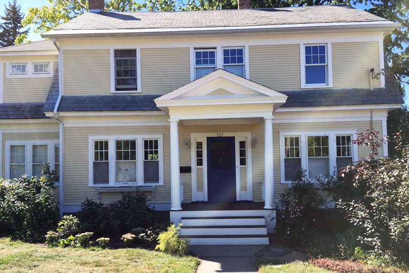A freshly painted pale yellow house with crisp white trim and a dark blue front door.